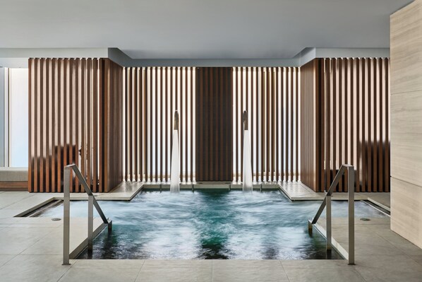 A modern indoor pool with a central water feature, flanked by wooden slats and metal railings.