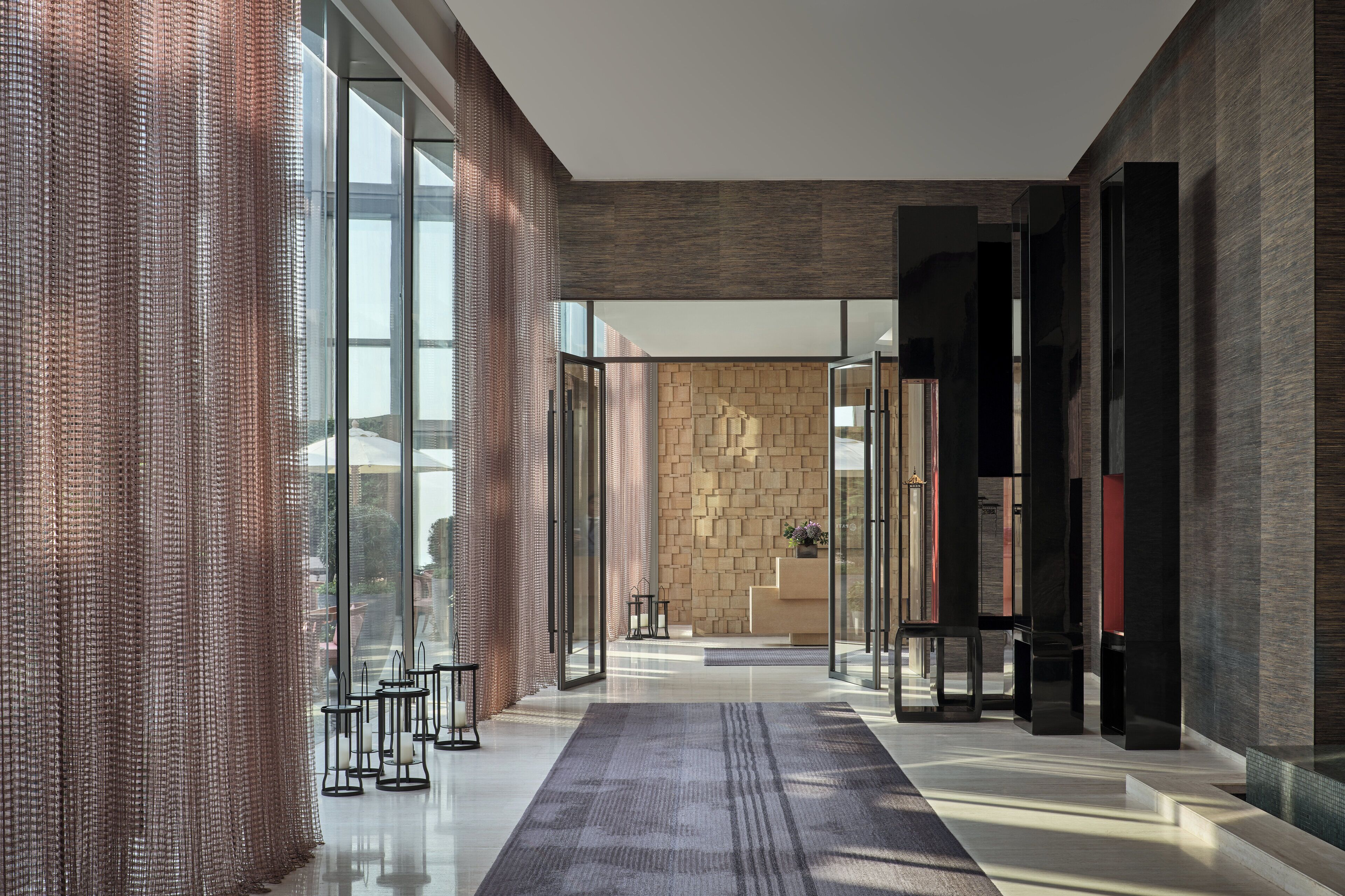 A modern lobby with a glass partition, a patterned wall, and a reception desk.