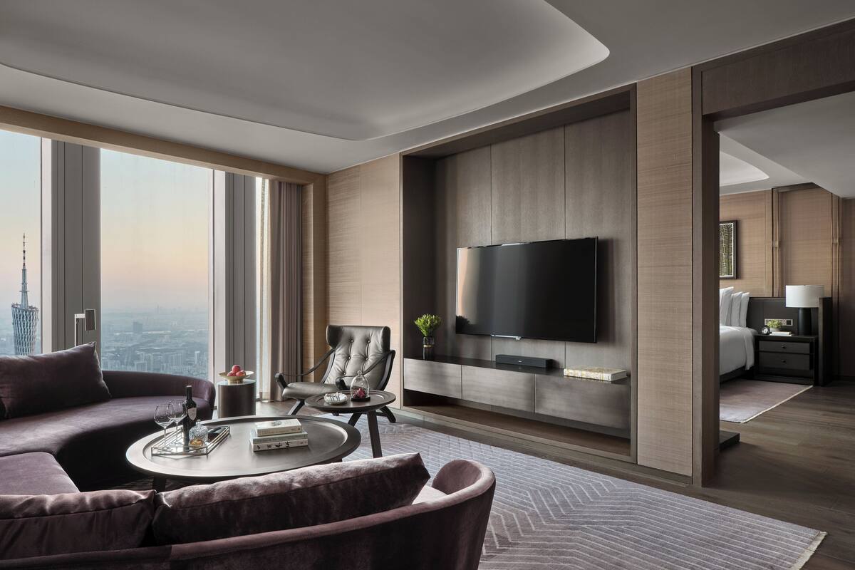Una habitación de hotel moderna con un ventanal grande, un televisor de pantalla plana, un sofá, una mesita de centro y una cama.