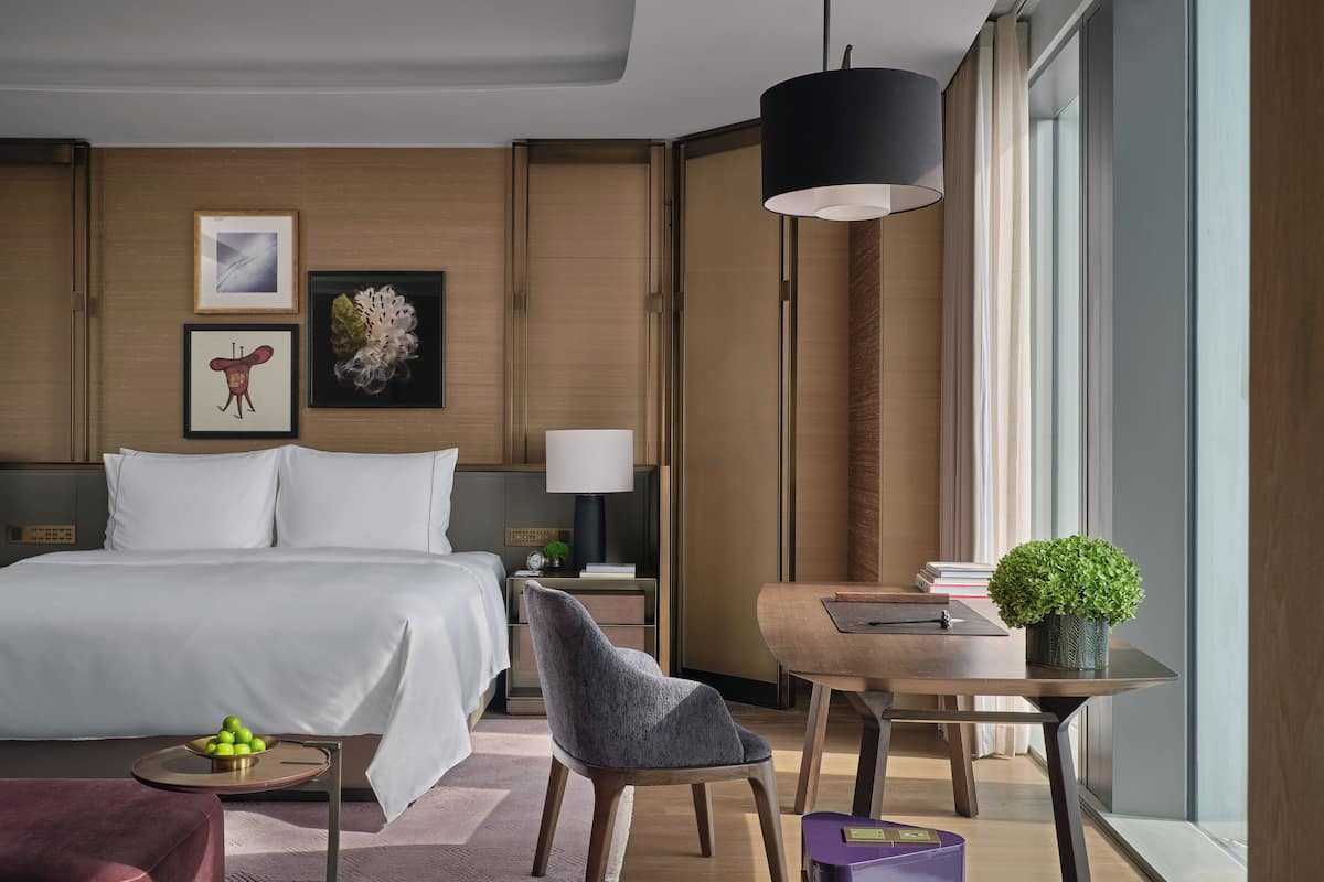 Una habitación de hotel moderna con una cama grande, un escritorio, una silla y una pequeña mesa con una planta.