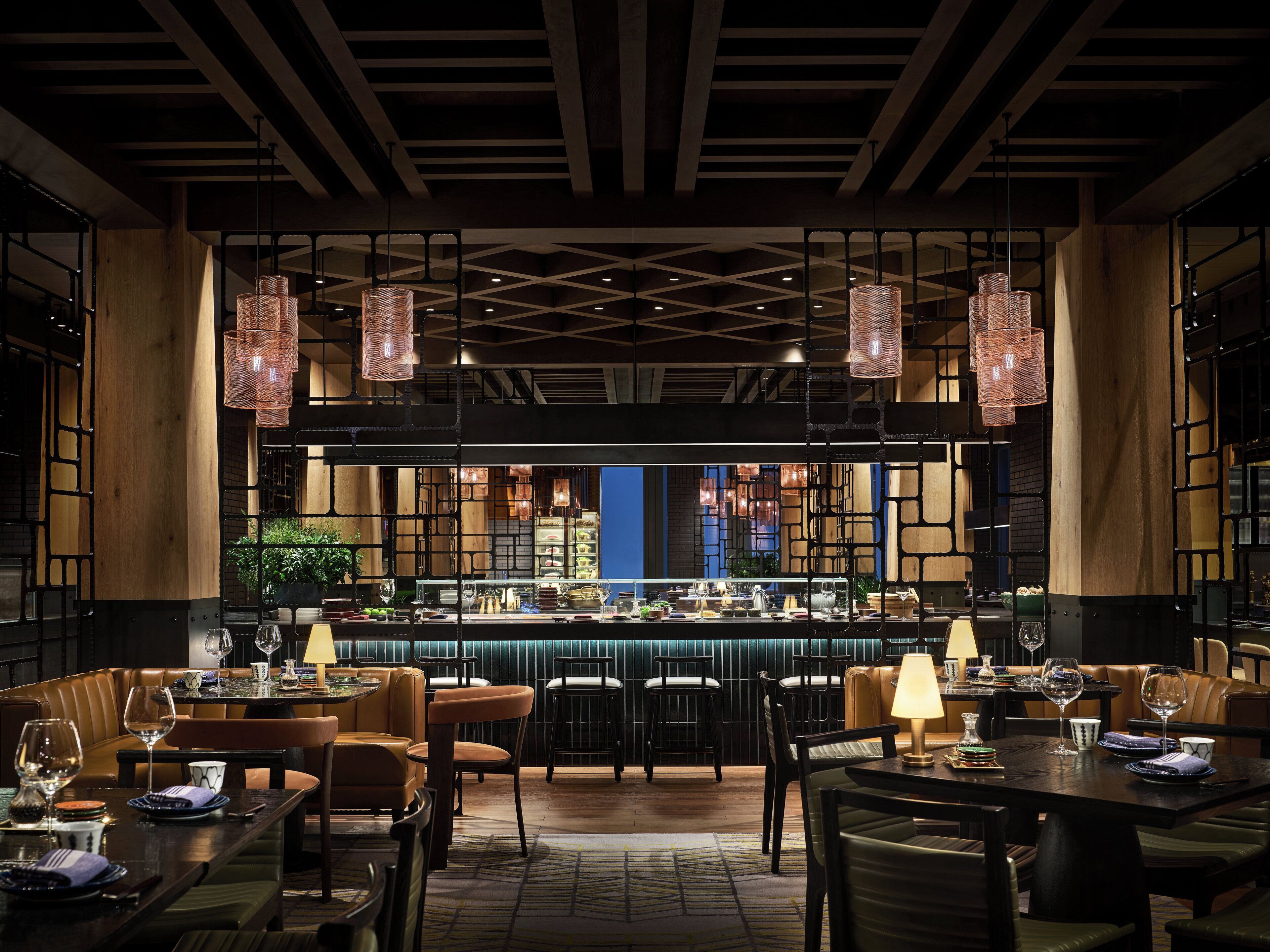 Um restaurante com área de bar, mobiliário de madeira e luminárias pendentes.