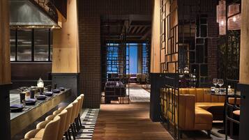 A modern restaurant with a long counter, multiple seating areas, and a view of the cityscape.
