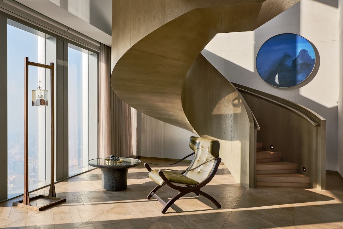 Un interior moderno con una escalera de caracol, una mesa redonda con superficie de vidrio y una silla con asiento acolchado.