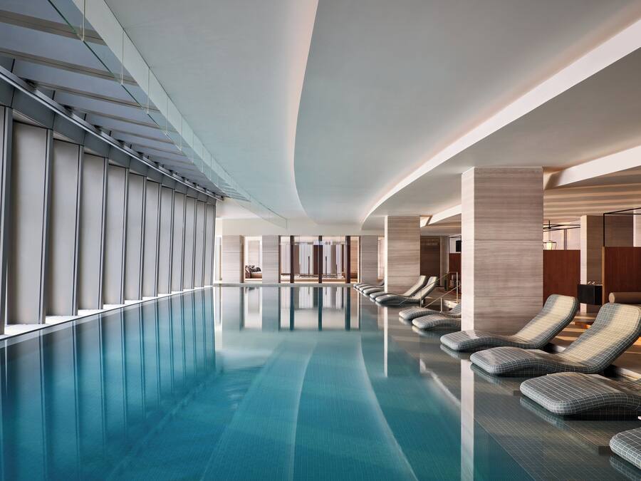 Una piscina interior moderna con un diseño largo y rectangular, y sillones de descanso a lo largo de un lado.
