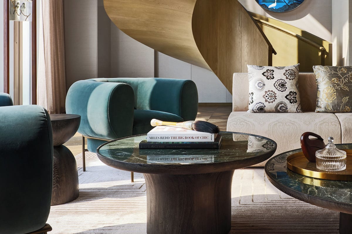 Una sala de estar moderna con techo de madera curva, un cuadro redondo que representa un paisaje de montaña y un sofá con cojines estampados.