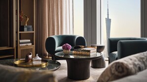 Ein modernes Wohnzimmer mit Blick auf ein hohes Gebäude, einem Bücherregal, zwei Sesseln und einem Couchtisch mit Dekoration.