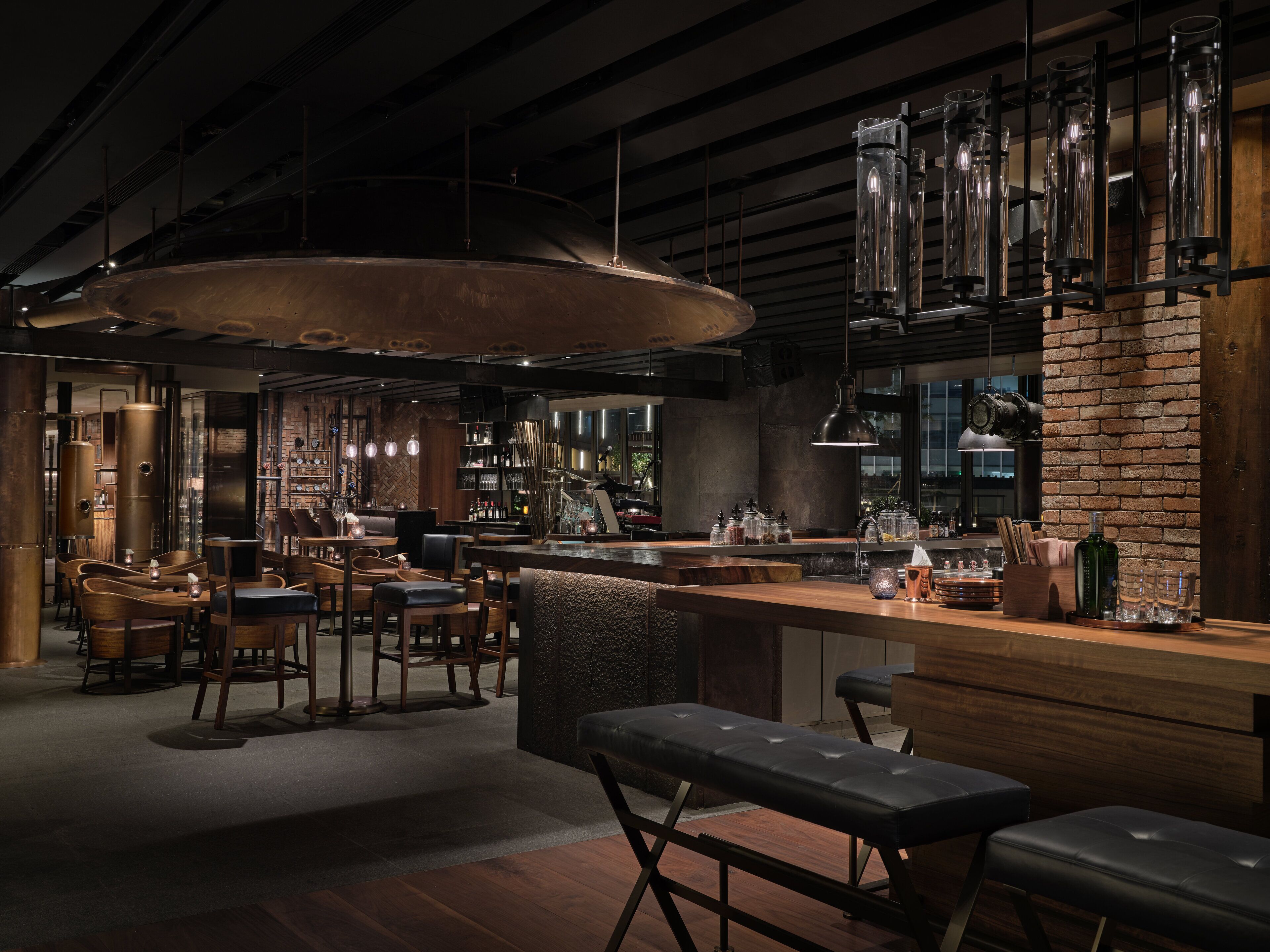 A modern bar area with wooden furniture, metal accents, and a brick wall.
