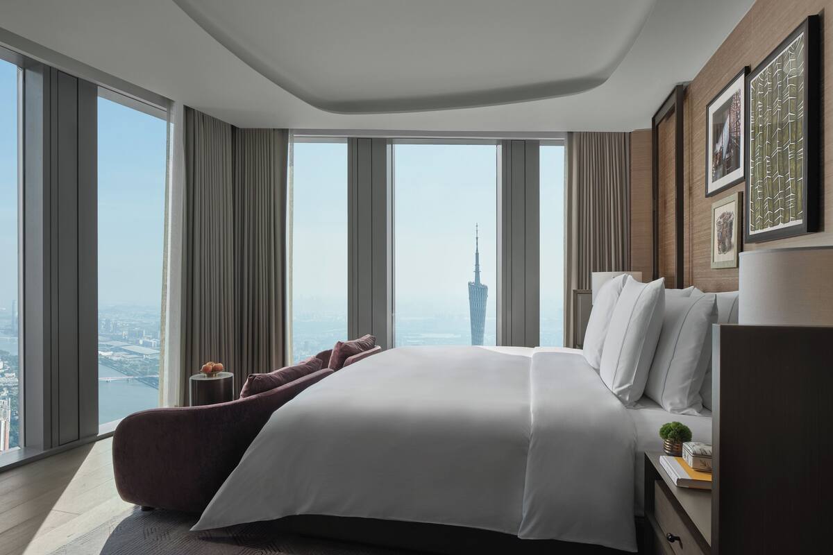 Una habitación de hotel moderna con una cama grande, una mesita de noche y vistas a un paisaje urbano que incluye un edificio alto.