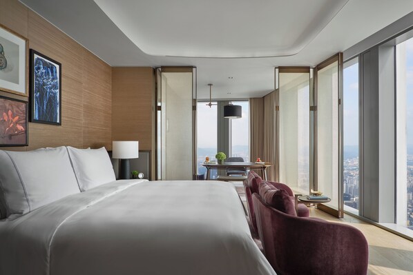 Une chambre d’hôtel moderne dotée d’un grand lit, d’un bureau, d’une chaise et offrant une vue sur la ville grâce à de grandes fenêtres.
