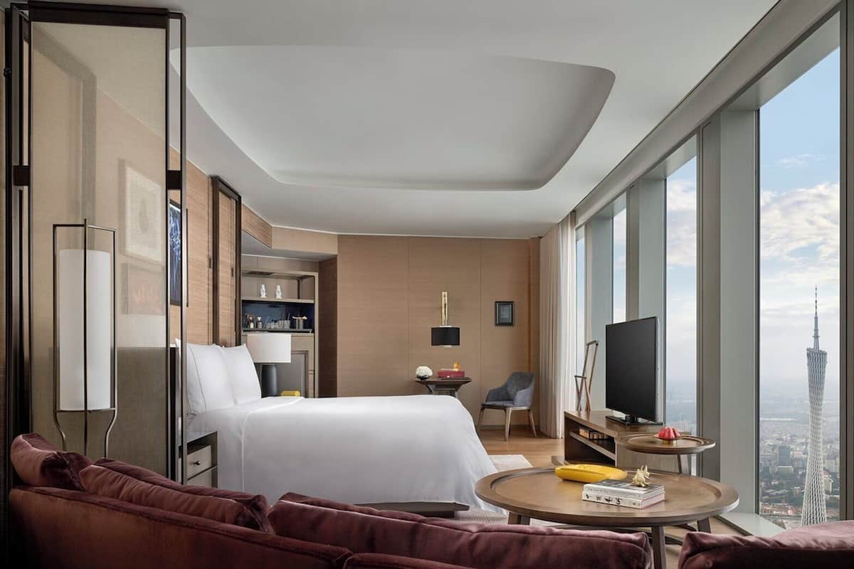 Habitación de hotel moderna con una cama grande, un sofá, una mesita, un televisor y vistas a la ciudad.