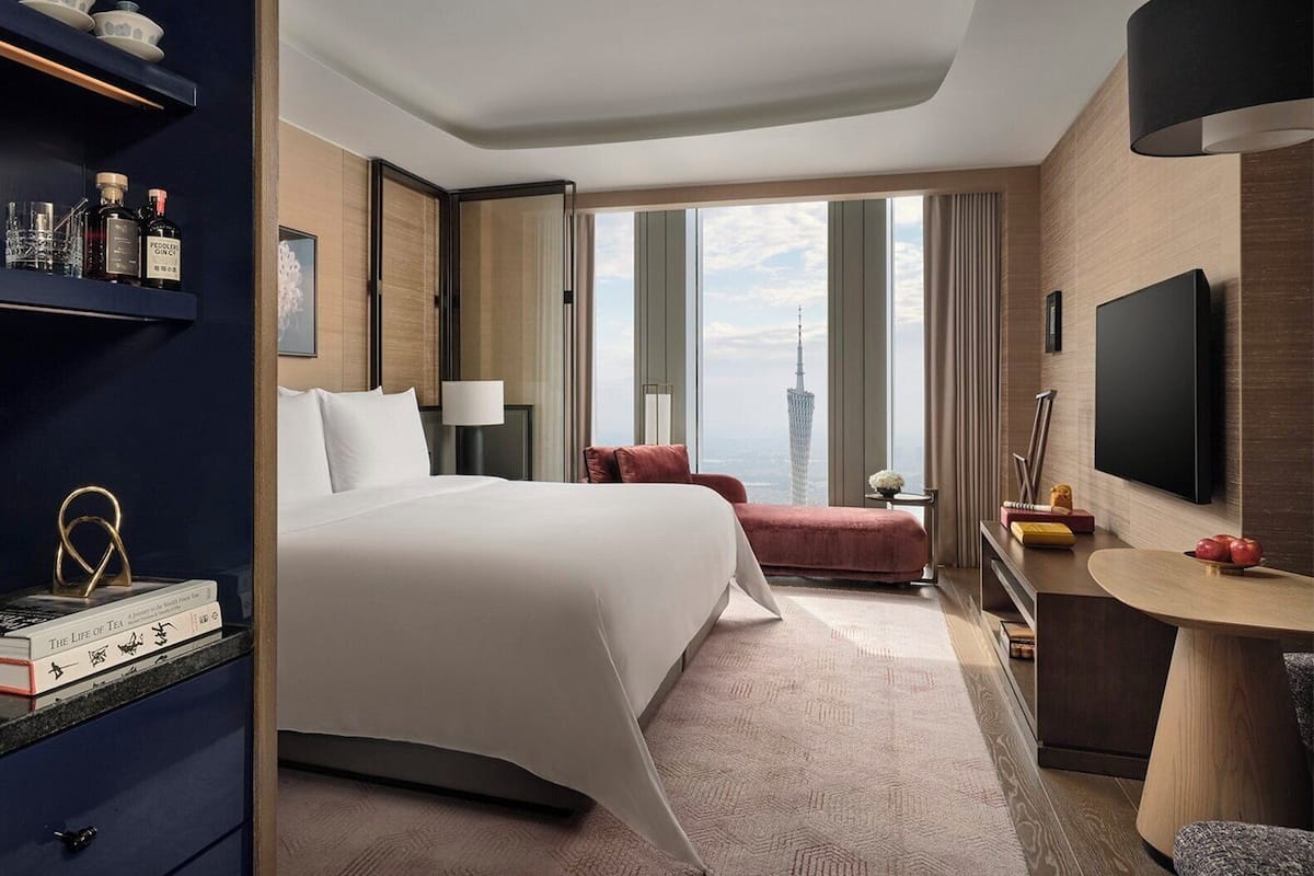 Habitación de hotel con una cama grande, un escritorio, televisión y vistas a un paisaje urbano.