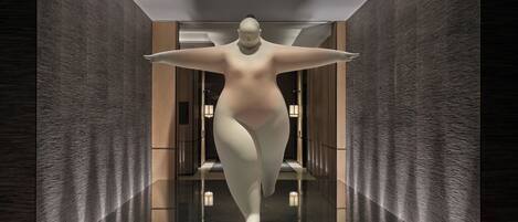 Un interior moderno con diseño minimalista, que presenta una gran escultura abstracta en el centro de un pasillo con paredes texturizadas y piso reflectante.