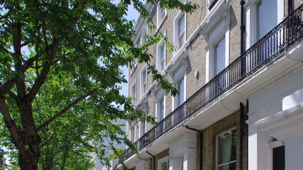 A row of white townhouses with black wrought iron fences, a tree-lined sidewalk, and a clear sky. - The London Agent Chelsea Peaceful (London)