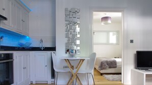 A modern kitchen with white cabinets, a dining table with chairs, and a small TV on a white stand. - The London Agent Chelsea Peaceful (London)