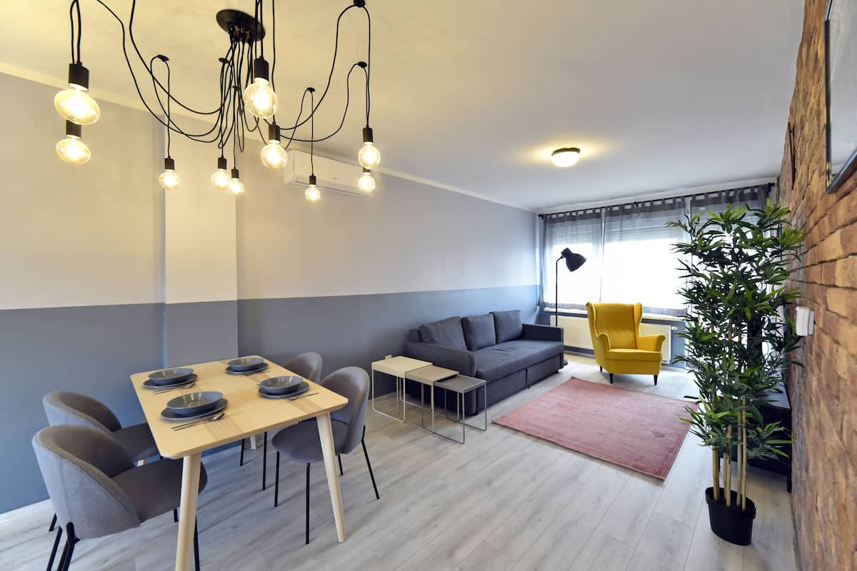 A modern living room with a dining area, grey sofa, yellow armchair, and a potted plant.