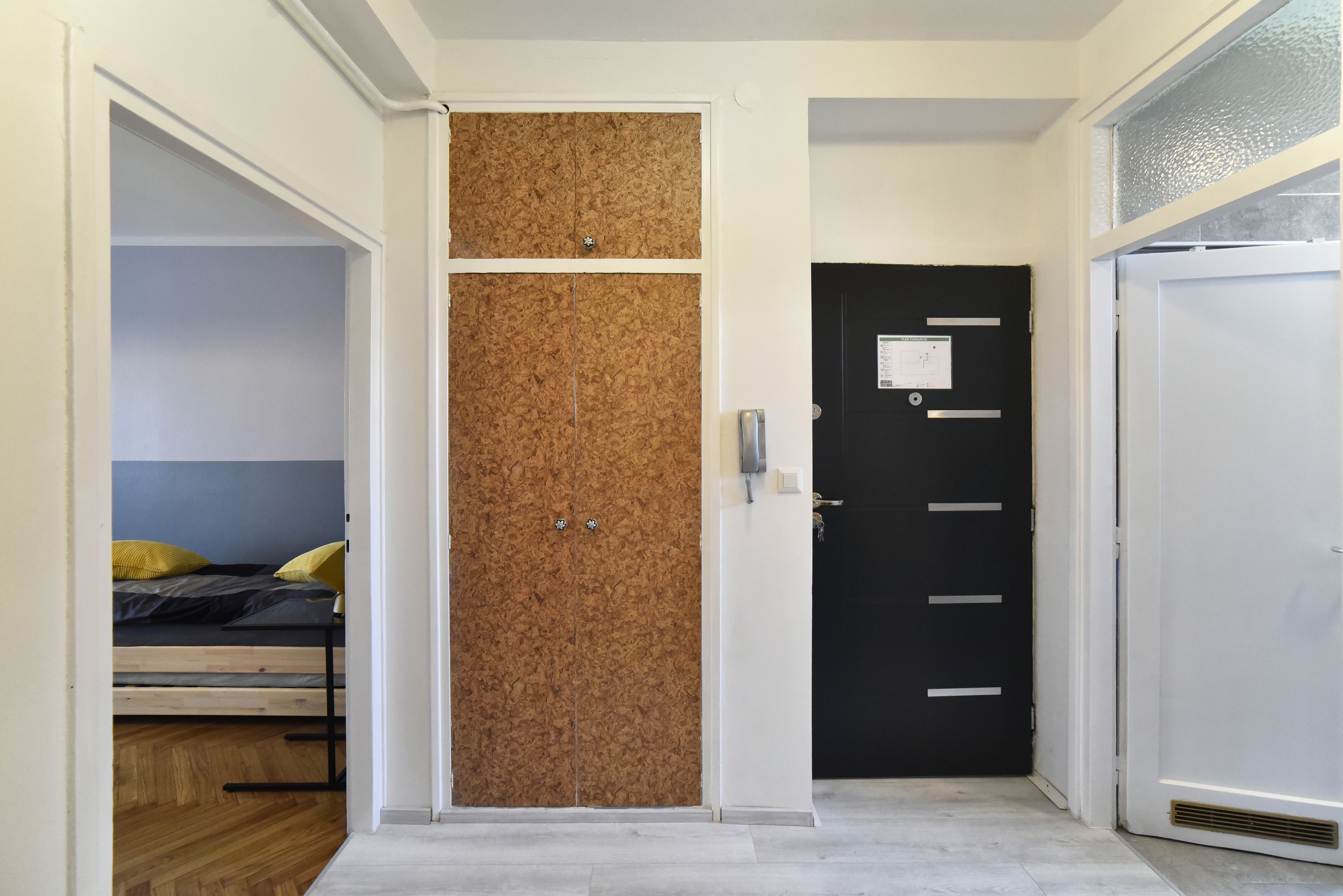 A room with a bunk bed, a corkboard wall, a black door with a lock, and a white door with a vent.