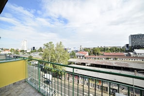 A view from a balcony overlooking a cityscape with buildings, a train station, and a clear sky.