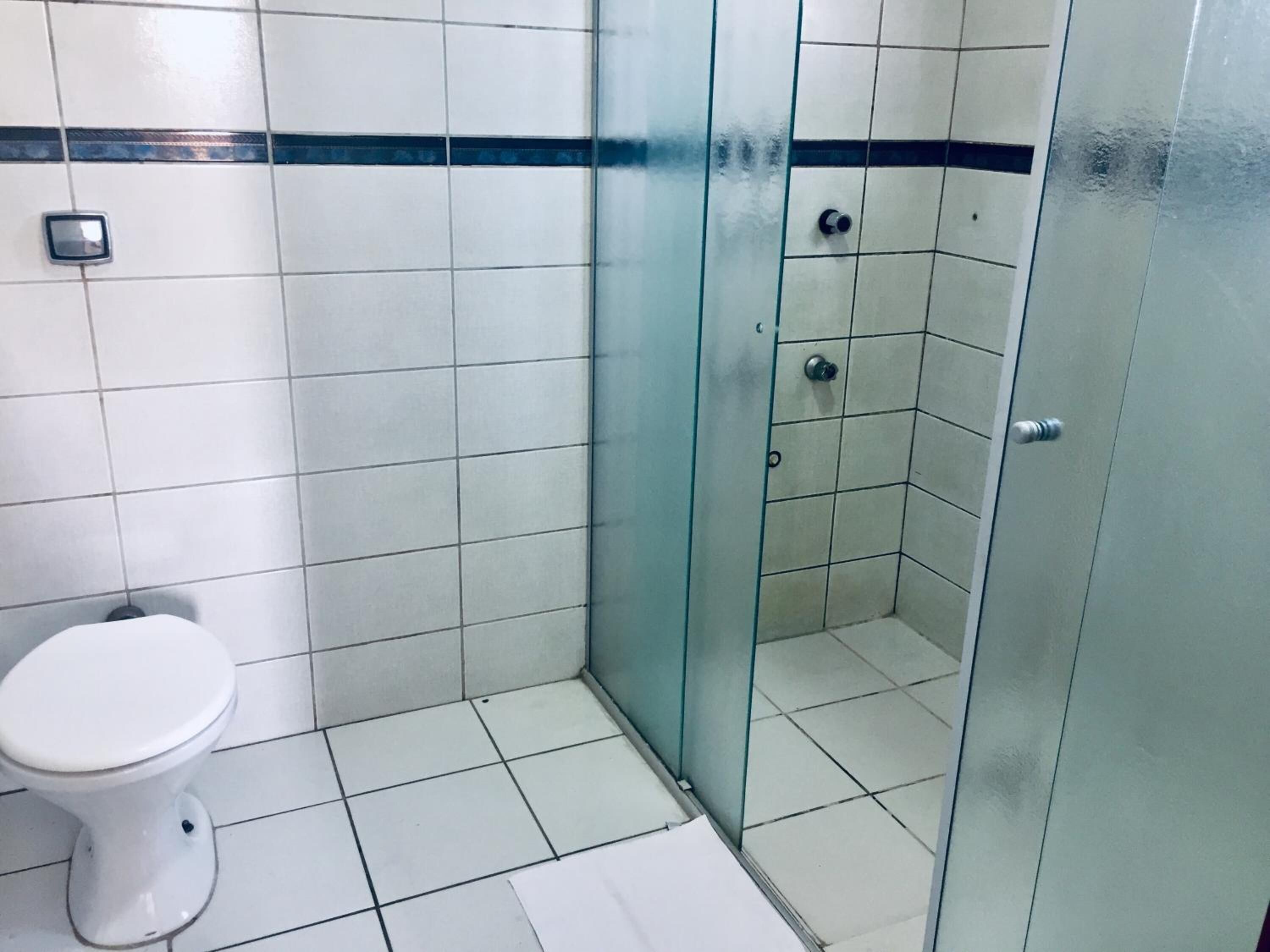 A bathroom with white tiles, a toilet, and a glass-enclosed shower area.