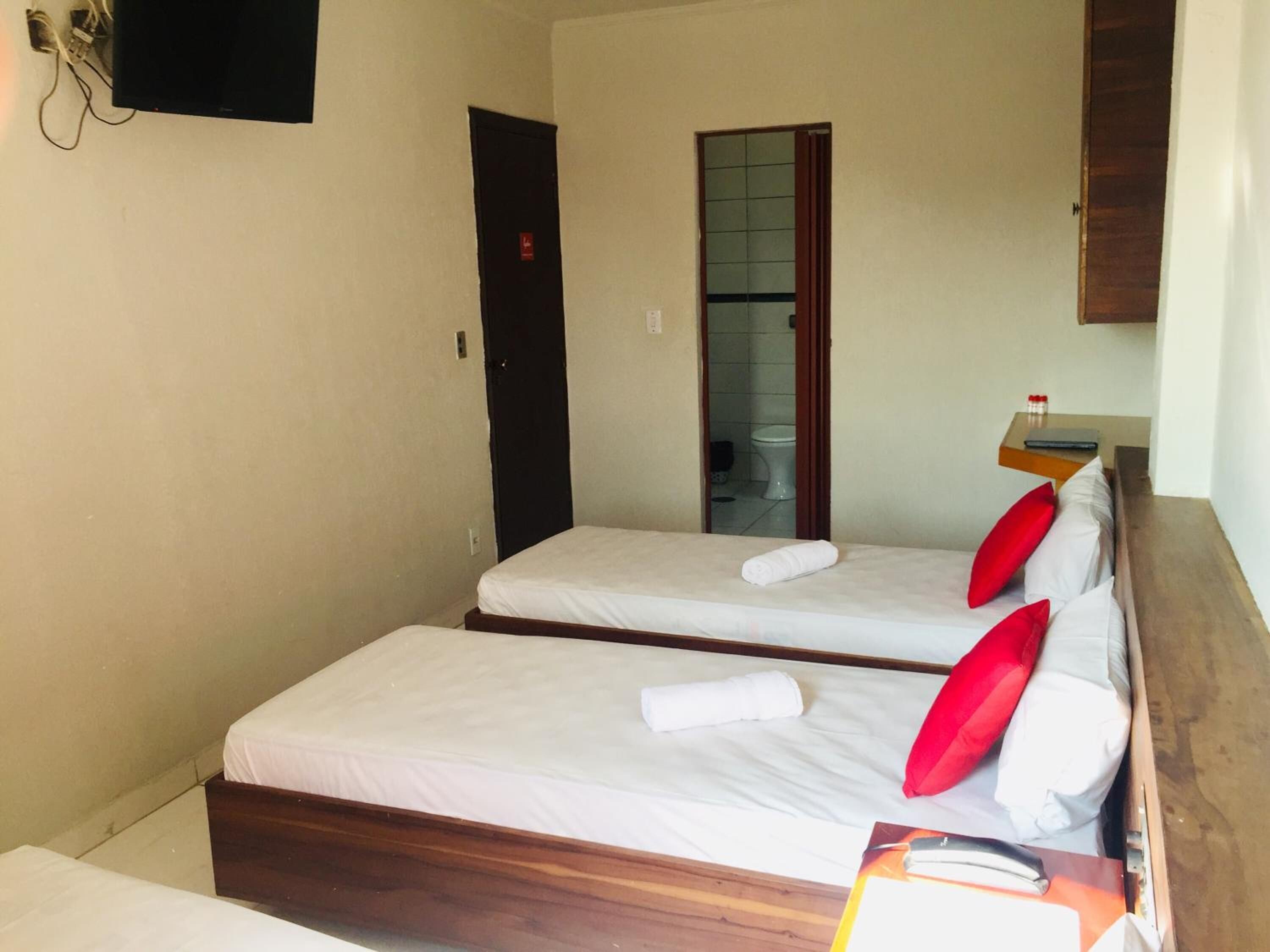 A hotel room with two single beds, a wooden headboard, a small bedside table with a book, and a mirror.