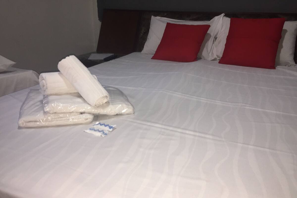 A neatly made bed with white linens, red pillows, and a folded towel on the side.