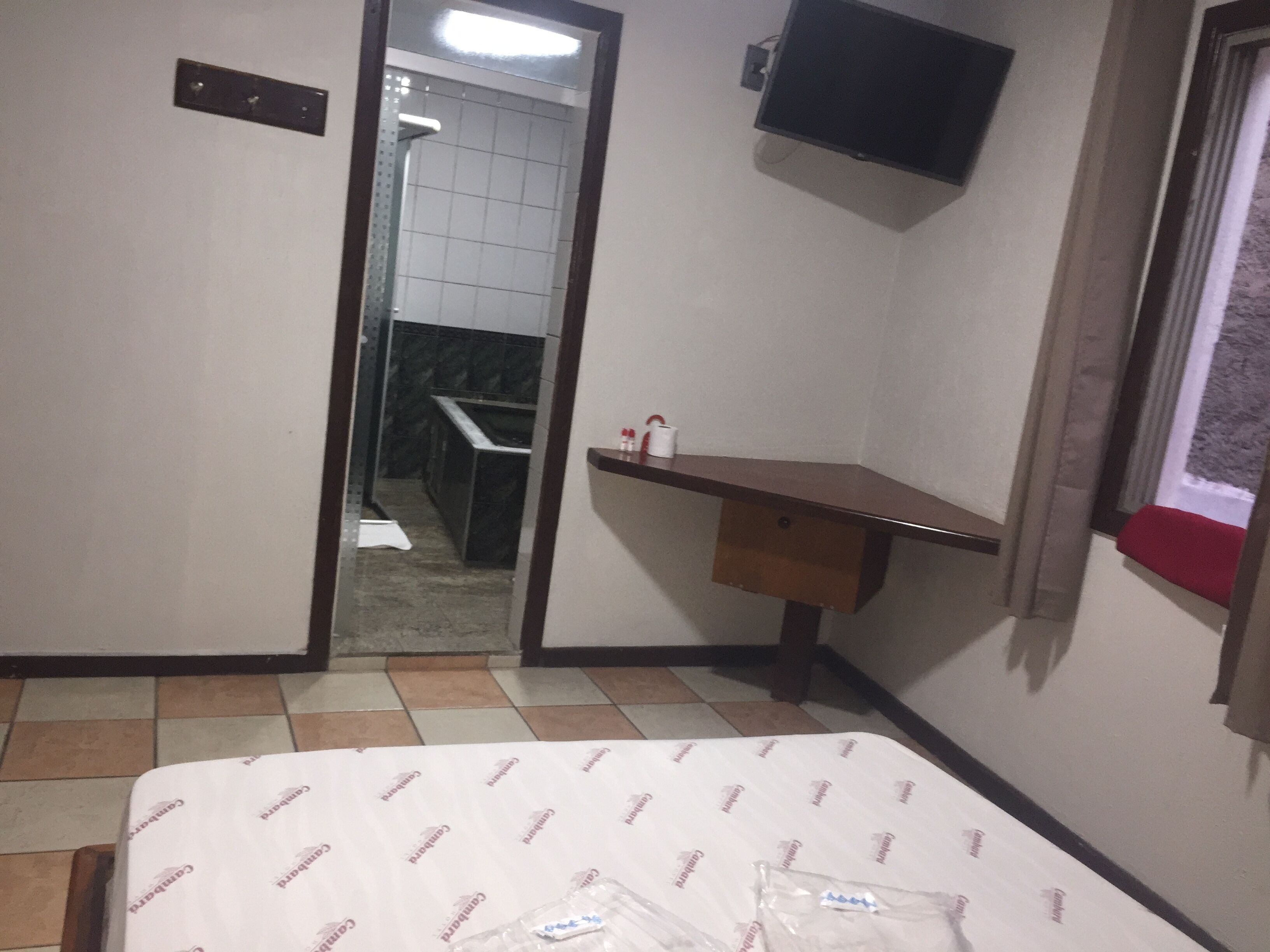 A hotel room with a bed, a small desk, a TV mounted on the wall, and a bathroom visible through an open door.
