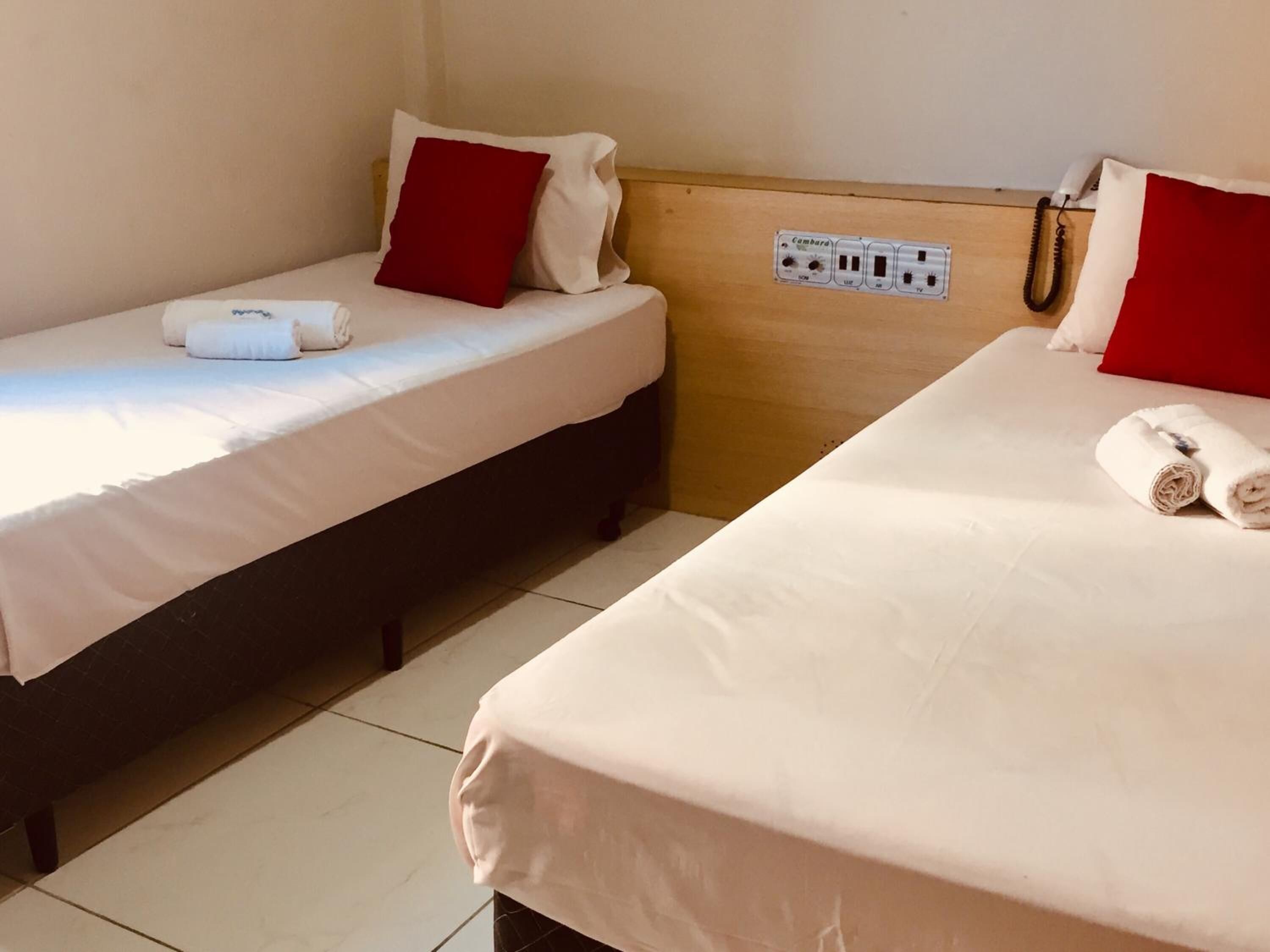 Two single beds with red pillows, white linens, and a wooden headboard with electrical outlets.