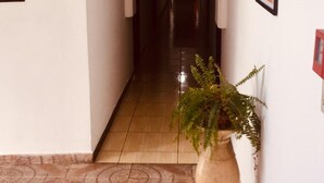 A hotel corridor with a directional sign for the emergency exit, a potted plant, and framed artwork on the walls. - Hotel Cambará (Osasco)