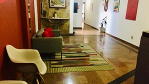 A hallway with a sofa, chairs, a patterned rug, and artwork on the walls. - Hotel Cambará (Osasco)