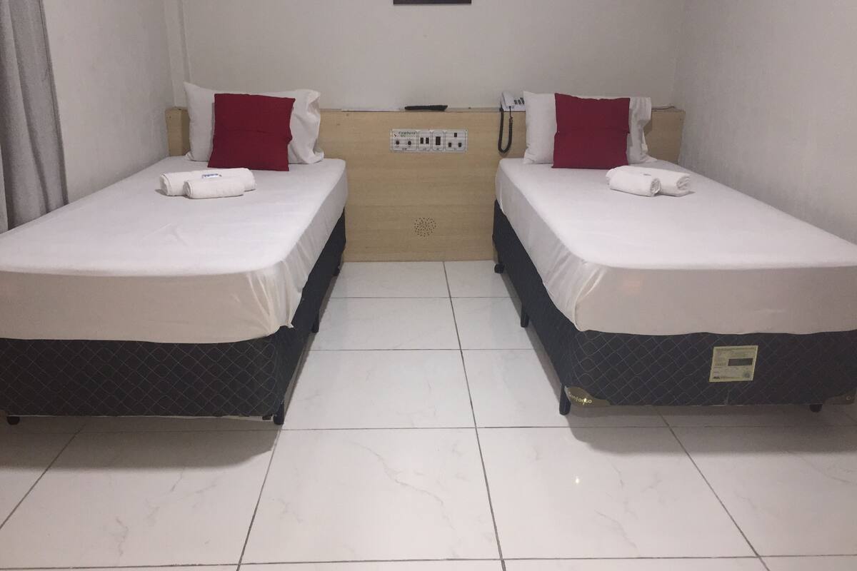 A hotel room with two single beds, a wooden headboard, a telephone, and a power outlet.