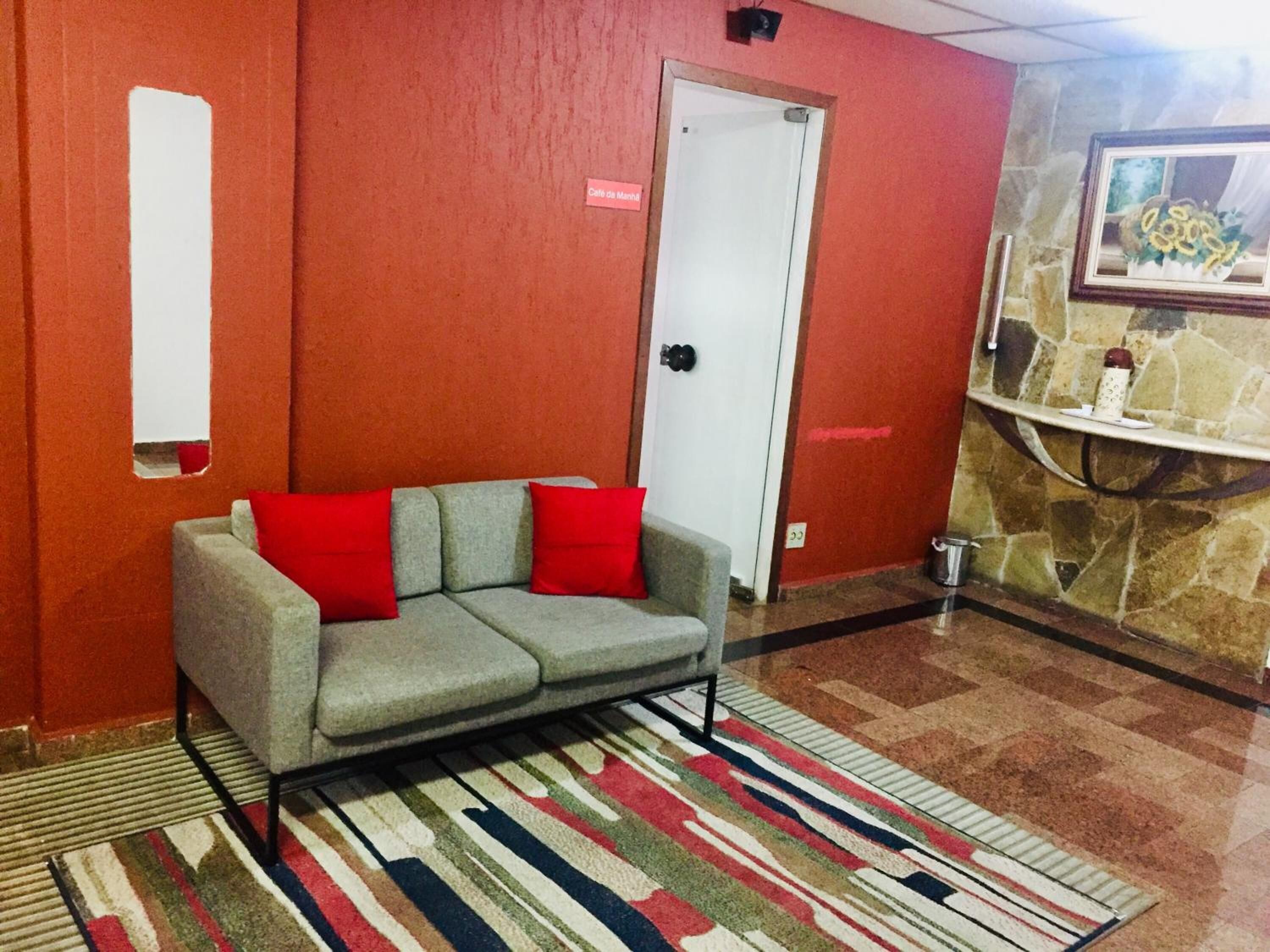A room with a grey sofa with red cushions, a striped rug, and a stone wall with a framed picture.