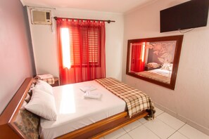 Een hotelkamer met een bed, een aan de muur bevestigde televisie en een raam met rode gordijnen.