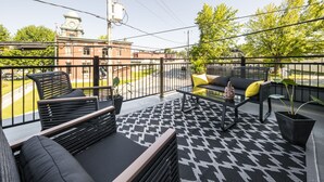 Een balkon met buitenmeubilair, een patroonrijk vloerkleed en uitzicht op een gebouw met een klokkentoren.
