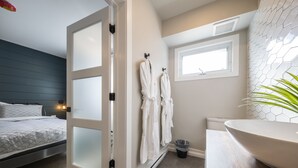 Een moderne badkamer met een grote witte wastafel, een raam en twee witte badjassen aan haken.