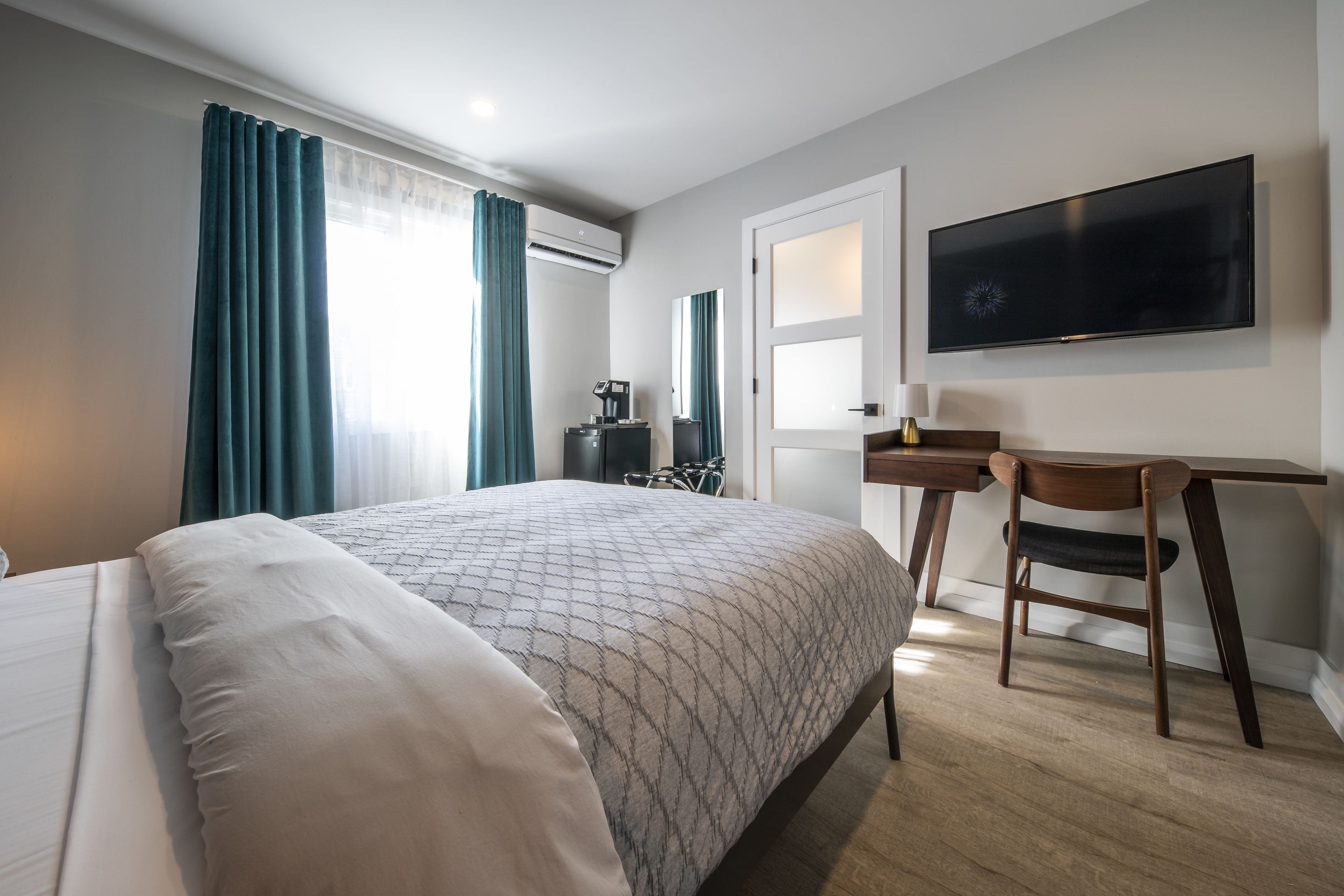Ein Hotelzimmer mit einem Bett, einem Schreibtisch, einem Sessel, einem Fernseher und einer Klimaanlage.