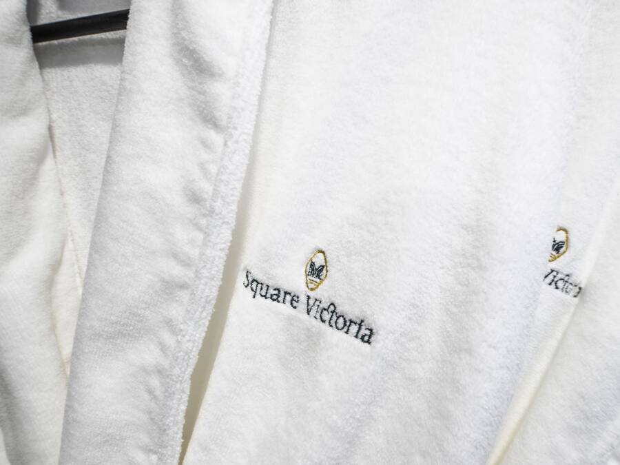 Toalha branca com bordado contendo o texto "Square Victoria" e um logotipo.