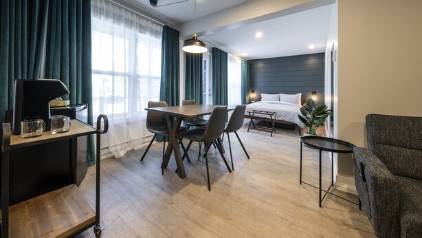 Een moderne hotelkamer met een houten eettafel, stoelen, een klein bijzettafeltje, een bed met hoofdbord en een bank.