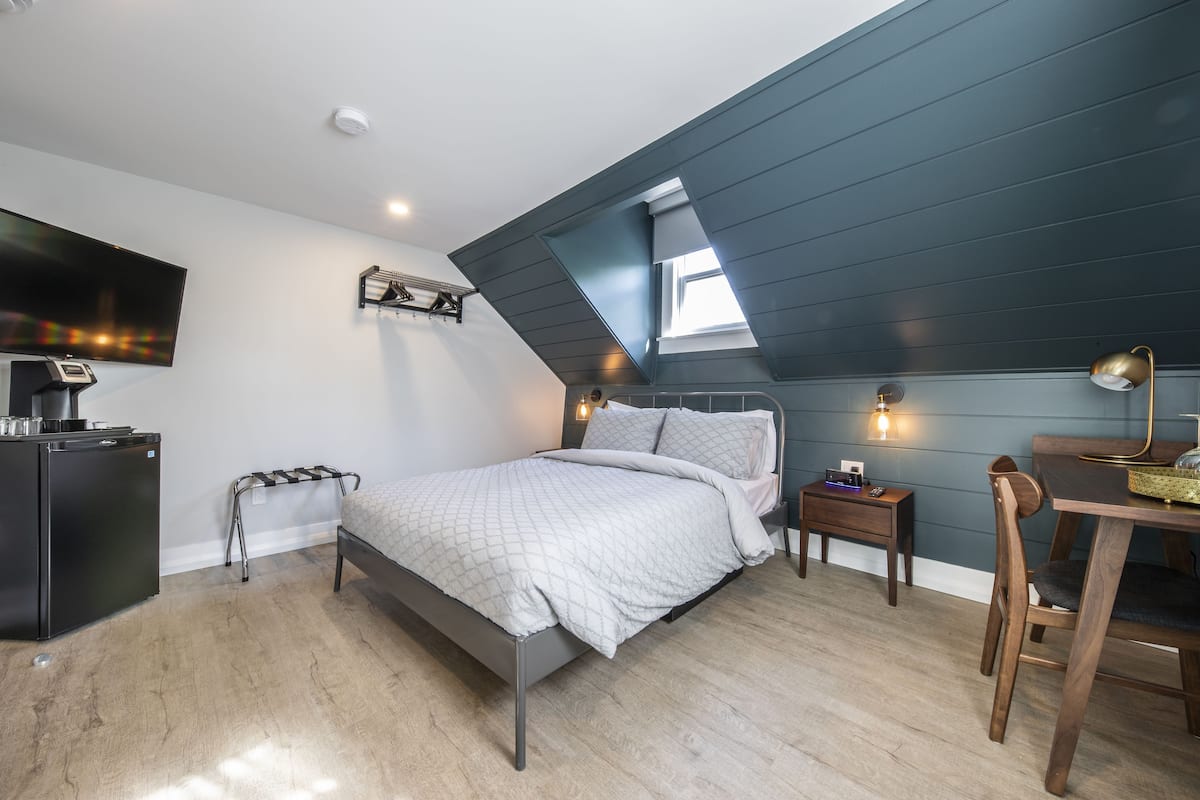 Ein Schlafzimmer mit Bett, Schreibtisch, Stuhl, Fernseher, kleinem Tisch und Fenster.