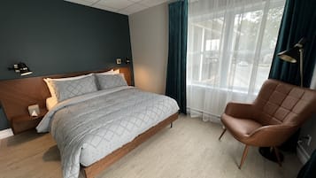 Quarto com cama, cadeira, mesa de cabeceira, luminária e janela com cortinas.