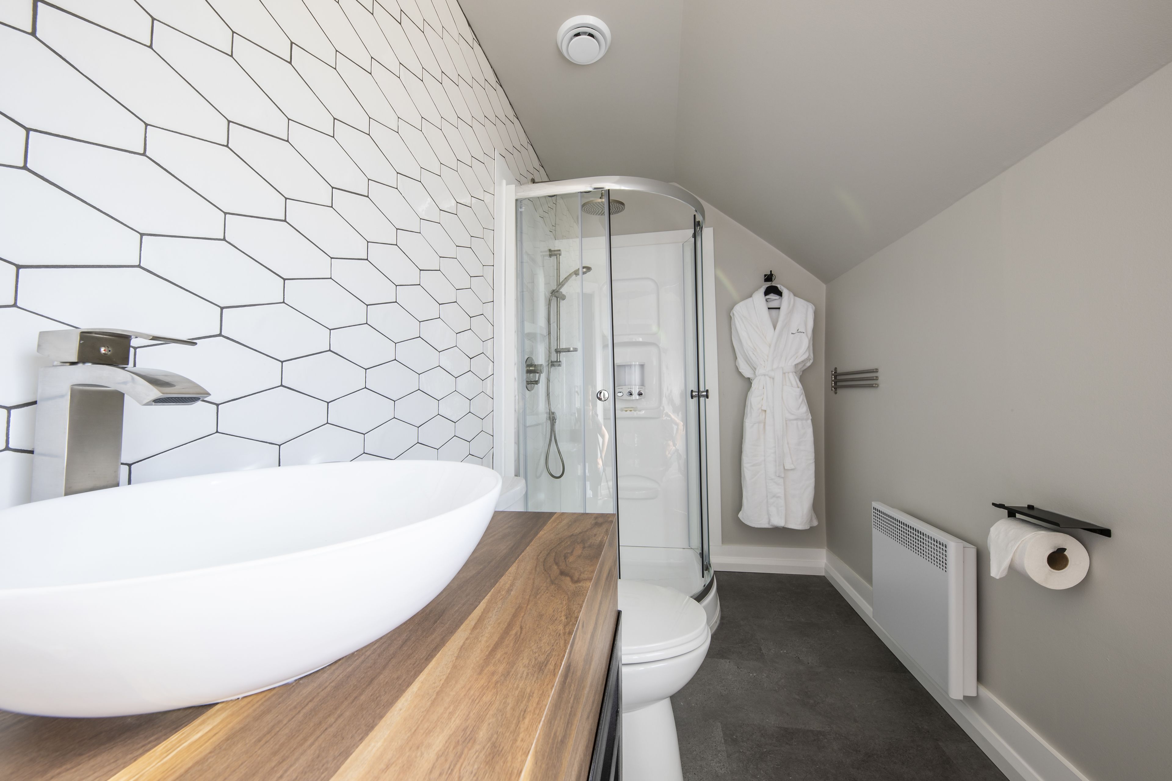 A modern bathroom with a large white vessel sink, a wooden countertop, a glass-enclosed shower, and a white toilet.