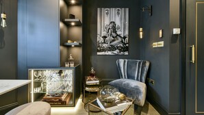 A modern living room with a dark wall, a blue armchair, a glass coffee table with books, and a framed artwork. - The London Agent Fulham Pied-a-Terre (London)
