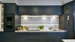 A modern kitchen with dark cabinetry, a marble backsplash, and under-cabinet lighting. - The London Agent Fulham Pied-a-Terre (London)
