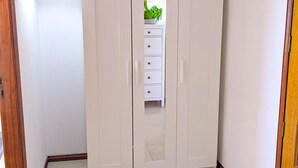 Una stanza con un ampio guardaroba bianco, un comò piccolo anch'esso bianco e una porta in legno.