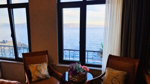 A room with two leather chairs, a small table with a vase of flowers, and large windows overlooking a body of water. -  Yalı Bahçe Mudanya (Mudanya)