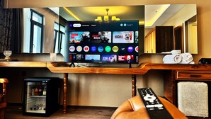 A hotel room with a large flat-screen TV mounted on a wooden console, a mini-fridge, and a remote control on a leather ottoman. -  Yalı Bahçe Mudanya (Mudanya)