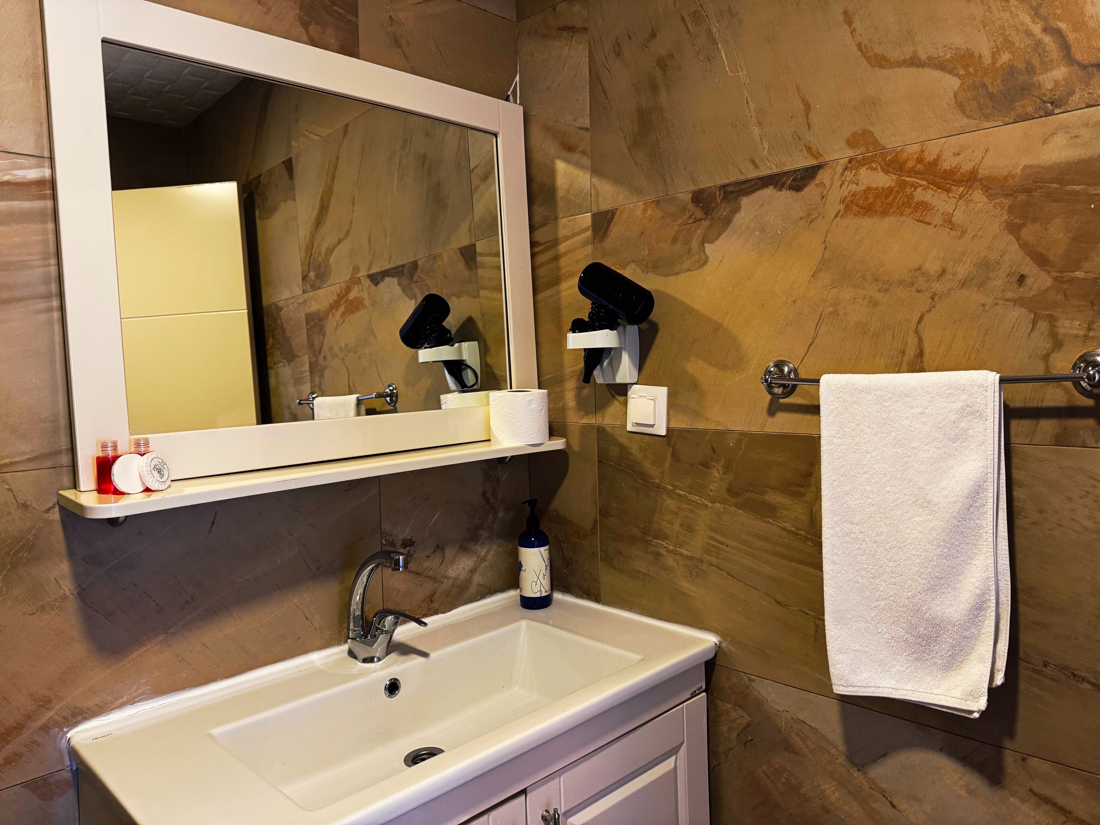 Une salle de bain avec un lavabo blanc, un miroir, un porte-serviettes et des articles de toilette.