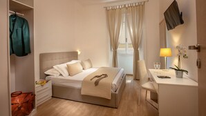A hotel room with a bed, bedside table, desk, chair, TV, and a window with curtains. - Domus Veneto Rome (Rome)