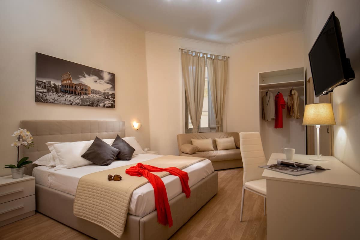 Ein Hotelzimmer mit Bett, Sofa, Schreibtisch, Fernseher und einem Fenster mit Vorhängen.