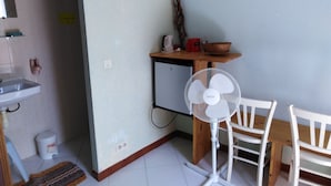 A small kitchen area with a sink, a white fan, a wooden table, and a chair. - Single room 2 person motel 2 (Porto-Vecchio)