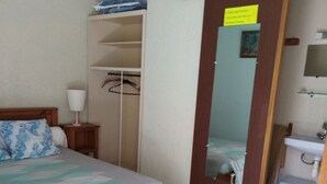 A bedroom with a bed, a wardrobe, a mirror, a bedside table, and a bathroom with a sink and a stool. - Single room 2 person motel 2 (Porto-Vecchio)