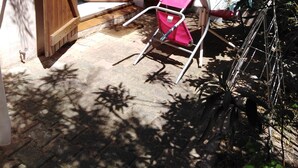 A wooden gate leading to a covered entrance with a patterned curtain, a pink folding chair, and a bicycle leaning against a metal fence. - Single room 2 person motel 2 (Porto-Vecchio)